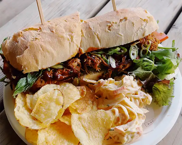 A big pulled pork sandwich and crisps on a paper plate made by the Dutch Barn Kitchen