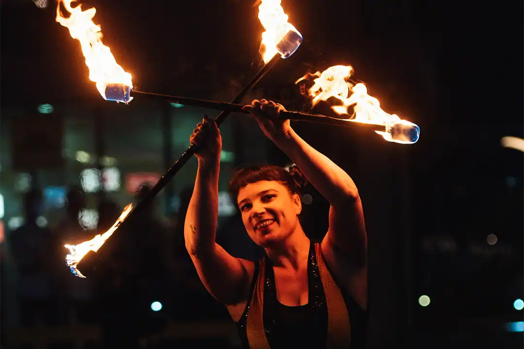 A fire dancer twirls two sticks, lit at both ends, above her head