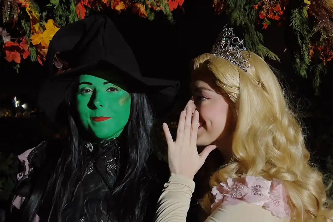 Glinda whispers to Elphaba who looks down the camera's lens