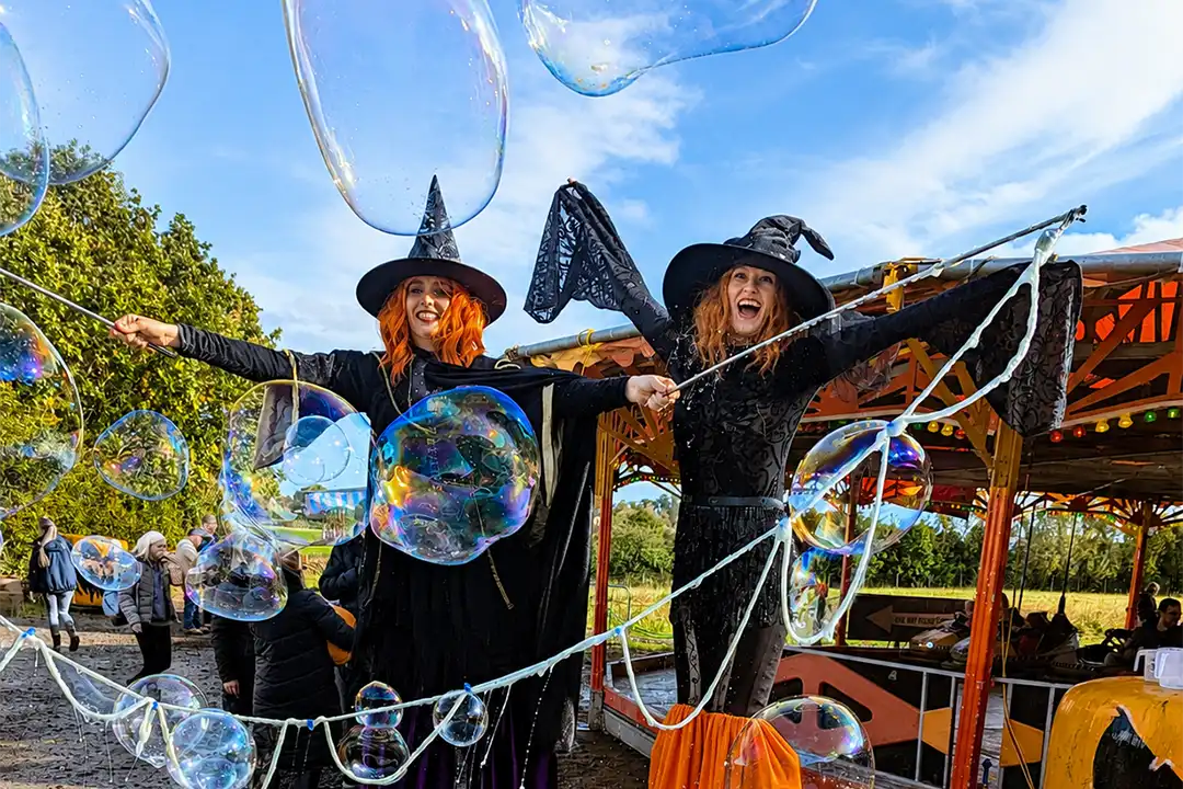 Stilt walkers dressed as witches blow big bubbles at Lillingstone Pick Your Own